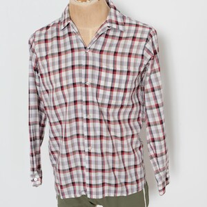 May include: A long-sleeved, button-down shirt with a plaid pattern in red, black, and white. The shirt is displayed on a mannequin and paired with olive green shorts. The shirt has a classic collar and buttoned cuffs.