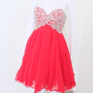 May include: A red strapless dress with a silver beaded bodice. The dress has a flowing skirt and a ruffled hem.