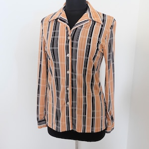 May include: A long-sleeve button-down shirt with a vertical striped pattern in tan, black, and white. The shirt has a pointed collar and is displayed on a black mannequin. The shirt's design is a mix of stripes and plaid.