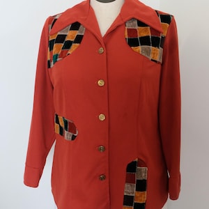 May include: A rust-coloured button-down shirt with long sleeves and a collar. The shirt features patchwork accents in various colours and textures on the chest and lower front. Gold-coloured buttons add a touch of elegance to the garment.