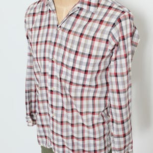 May include: A long-sleeved, button-down shirt with a classic plaid pattern in red, black, and gray on a white background. The shirt has a single chest pocket and is displayed on a mannequin.