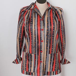 May include: A vintage shirt with a vertical stripe design in red, grey, beige and black. The shirt has a button-down front, long sleeves, and two front pockets. The pattern includes floral and polka dot details.