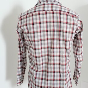 May include: A long-sleeved plaid shirt in a classic pattern. The shirt features a red, black, and gray checkered design on a white background. The shirt is button-down and has a collar.