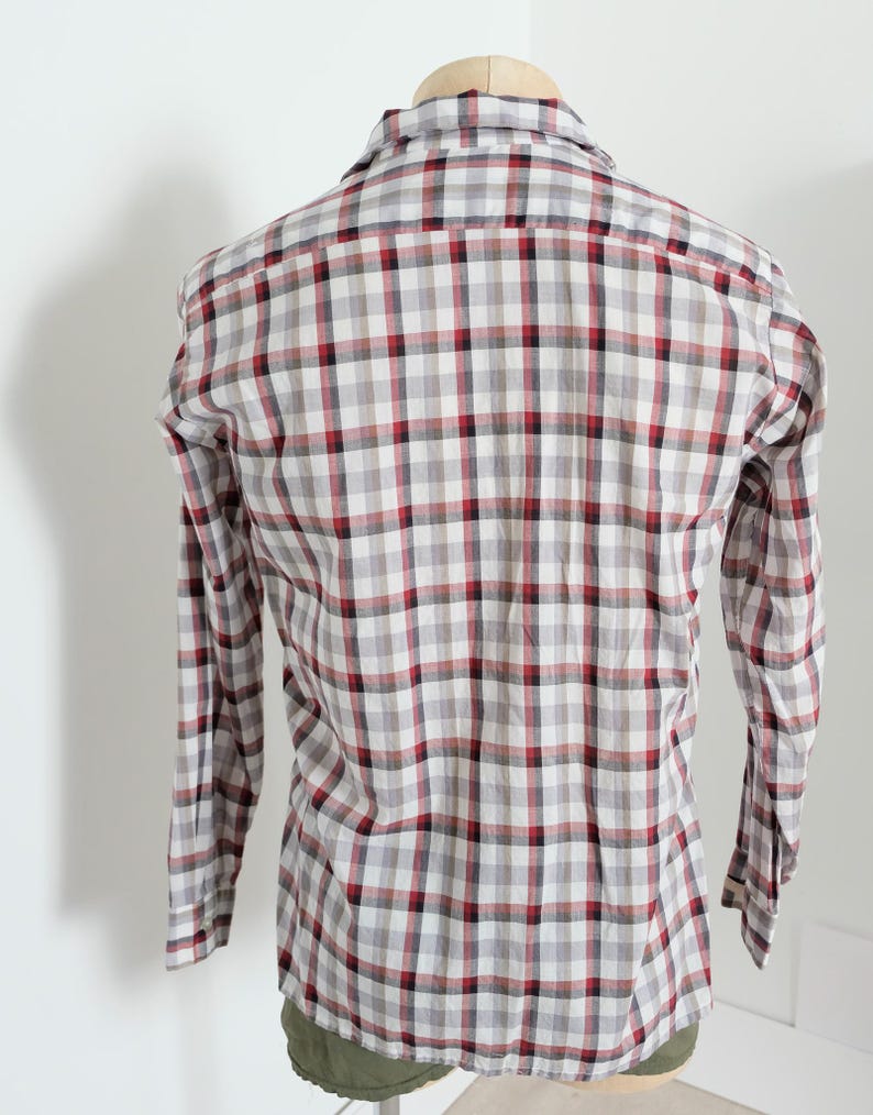 May include: A long-sleeved plaid shirt in a classic pattern. The shirt features a red, black, and gray checkered design on a white background. The shirt is button-down and has a collar.