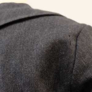 May include: Close-up of a dark gray wool jacket with a collar. The fabric has a subtle texture.