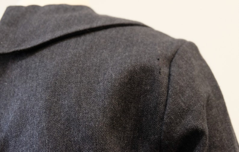 May include: Close-up of a dark gray wool jacket with a collar. The fabric has a subtle texture.