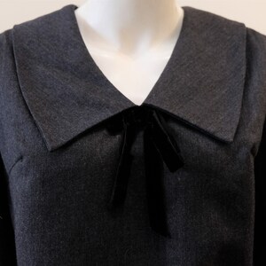 May include: A dark gray dress with a large, wide collar and a black velvet bow at the neckline.