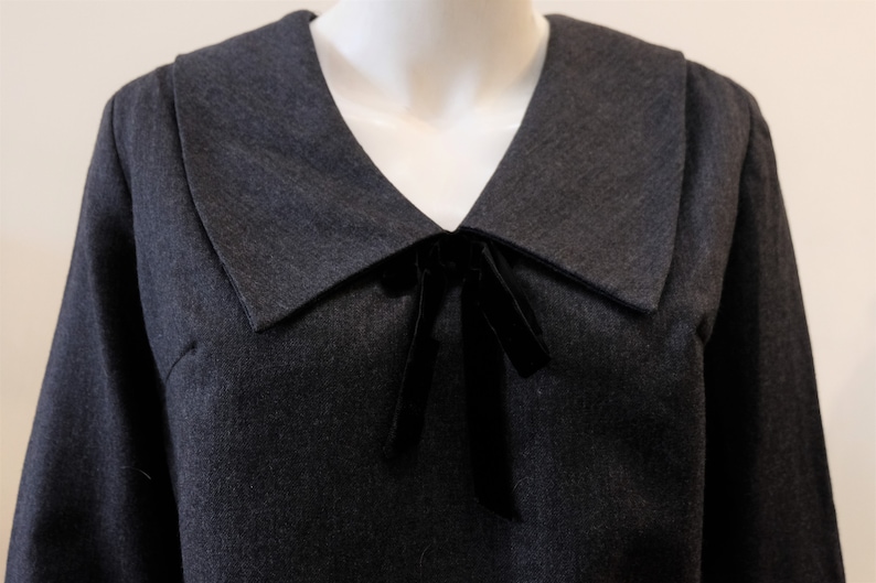 May include: A dark gray dress with a large, wide collar and a black velvet bow at the neckline.