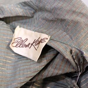 May include: A close-up of a green and gold striped fabric with a white tag that reads "Ellen Kaye".