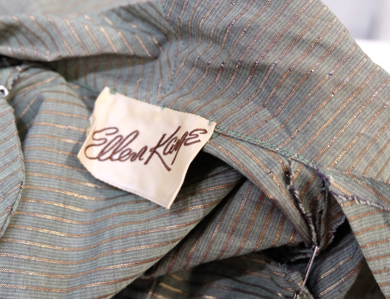 May include: A close-up of a green and gold striped fabric with a white tag that reads "Ellen Kaye".