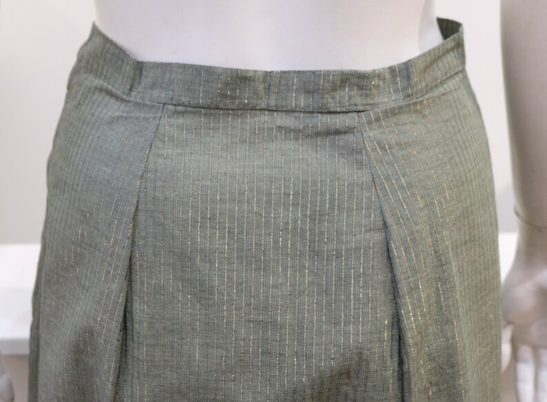 May include: A green skirt with thin gold stripes. The skirt has a waistband and a pleated front.