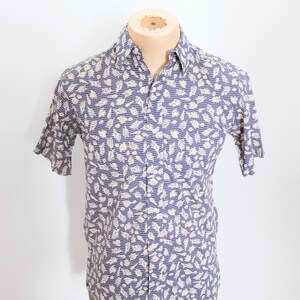 May include: A blue short-sleeved button-down shirt with a white seashell pattern.