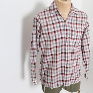 May include: A long-sleeved, button-down shirt in a classic plaid pattern. The shirt features a gray, red, and white checkered design. The shirt is displayed on a mannequin, showcasing its fit and style. The garment has a collared neckline and buttoned cuffs.