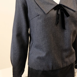 May include: A dark gray long-sleeved blouse with a wide collar and a black velvet bow at the neckline.