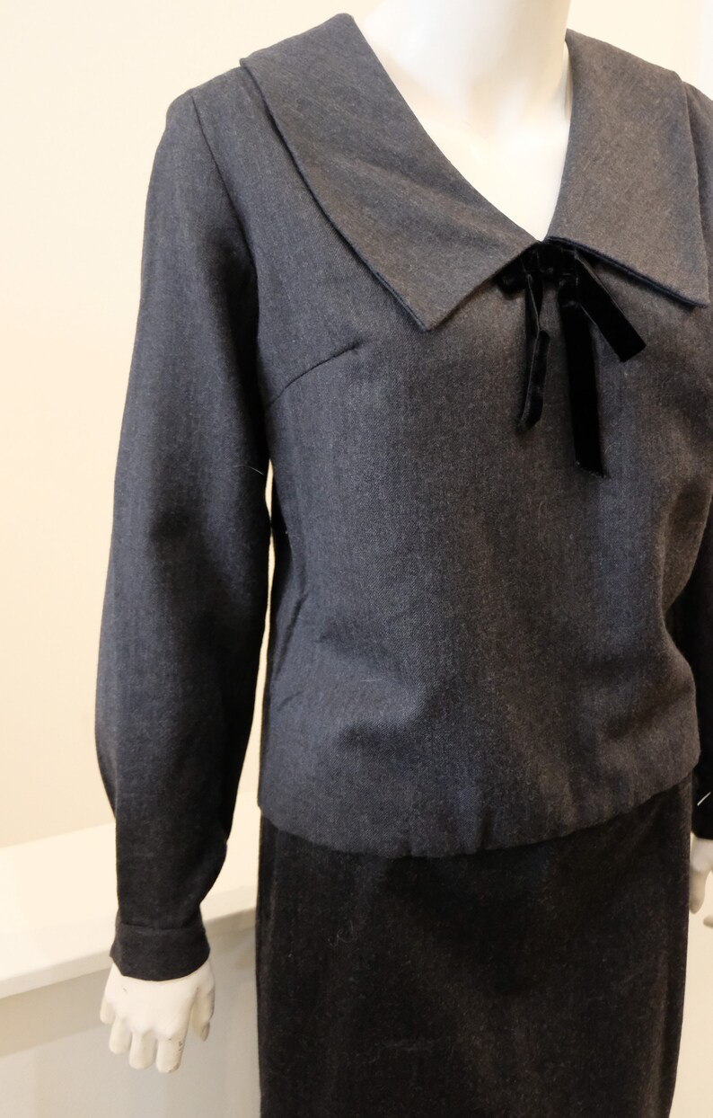 May include: A dark gray long-sleeved blouse with a wide collar and a black velvet bow at the neckline.