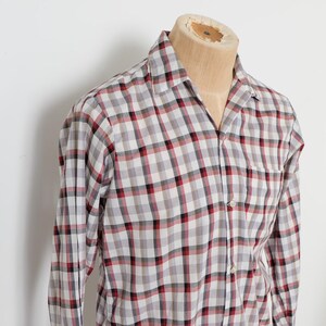 May include: A long-sleeved plaid shirt in a gray, red, and black pattern. The shirt is buttoned and has a collar. The shirt is displayed on a mannequin.