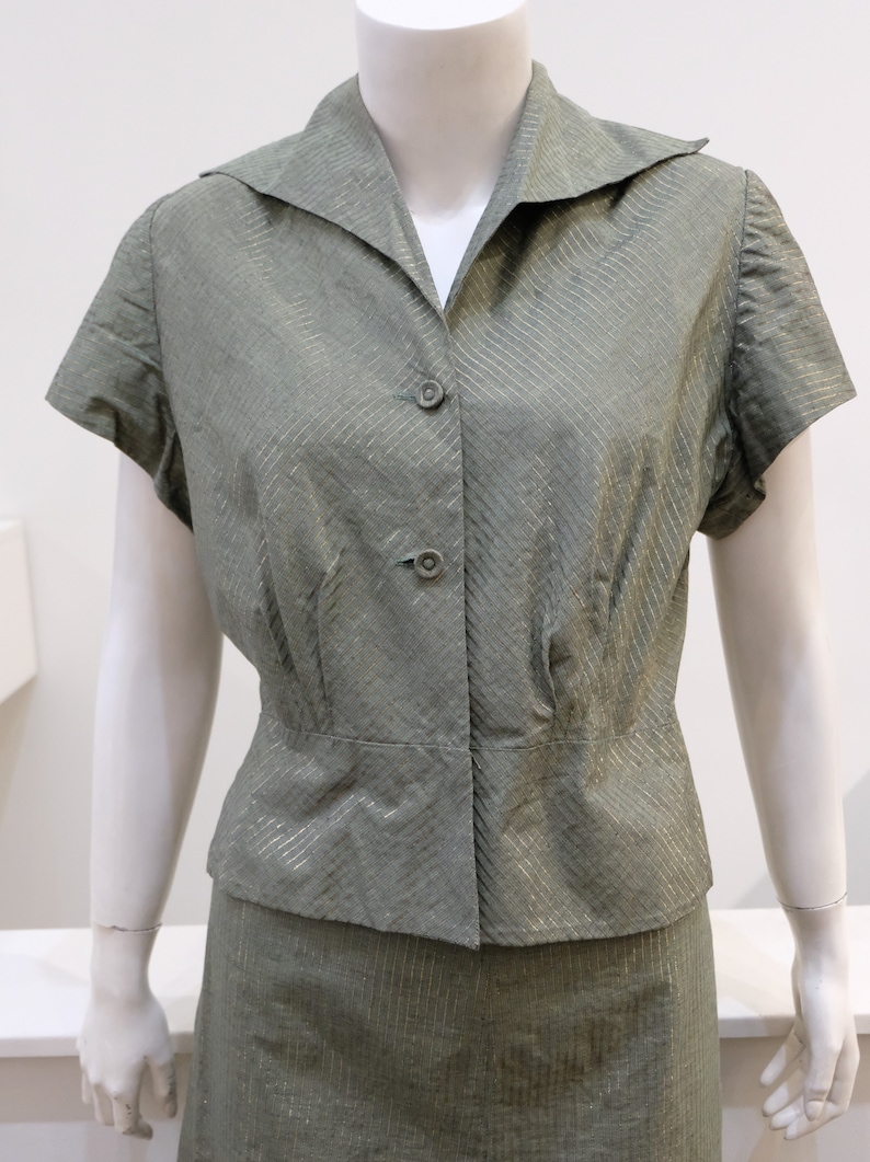 May include: A green and silver striped short-sleeved blouse and skirt set. The blouse has a collared neckline and button closure. The skirt is a-line and has a waistband.