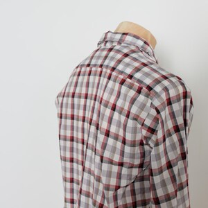 May include: A plaid button-down shirt in a gray, white, and burgundy color scheme. The shirt is displayed on a mannequin, showcasing the back and shoulder details. The pattern is a classic check design.