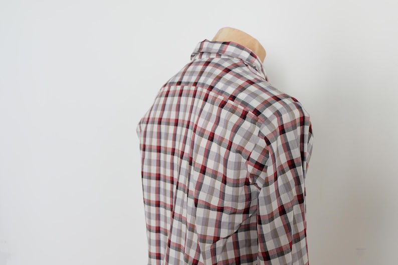 May include: A plaid button-down shirt in a gray, white, and burgundy color scheme. The shirt is displayed on a mannequin, showcasing the back and shoulder details. The pattern is a classic check design.