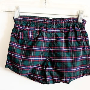 May include: Green, red, and white plaid swim trunks with an elastic waistband.