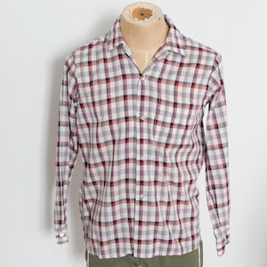May include: A long-sleeved, button-down shirt with a classic plaid pattern in red, black, and gray on a white background. The shirt is displayed on a mannequin. The shirt has a collared neckline and buttoned cuffs.