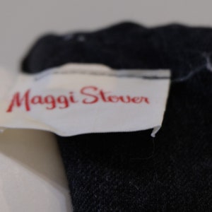May include: Close-up of a black zippered garment with a white label that reads "Maggi Stever".