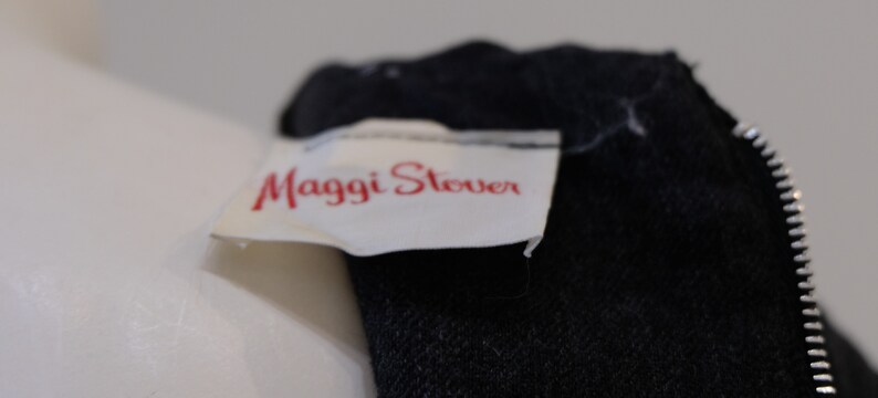 May include: Close-up of a black zippered garment with a white label that reads "Maggi Stever".