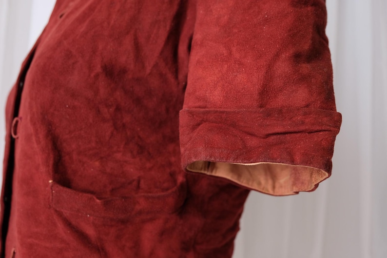 K&ouml;nnte beinhalten: Nahaufnahme einer rostfarbenen Jacke mit umgeschlagenem &Auml;rmel. Die Jacke hat eine Tasche und Kn&ouml;pfe vorne. Die Innenseite des &Auml;rmels ist hellbraun.