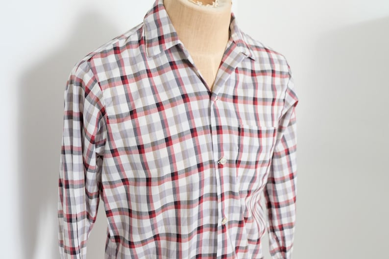 May include: A long-sleeved, button-down shirt with a plaid pattern in red, black, and white. The shirt is displayed on a mannequin and features a chest pocket and a classic collar.