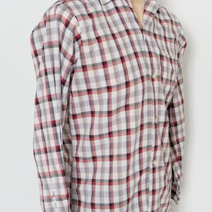 May include: A long-sleeved button-down shirt with a plaid pattern in white, gray, red, and black. The shirt is displayed on a mannequin and has a classic collar and buttoned cuffs. The shirt is paired with olive green shorts.