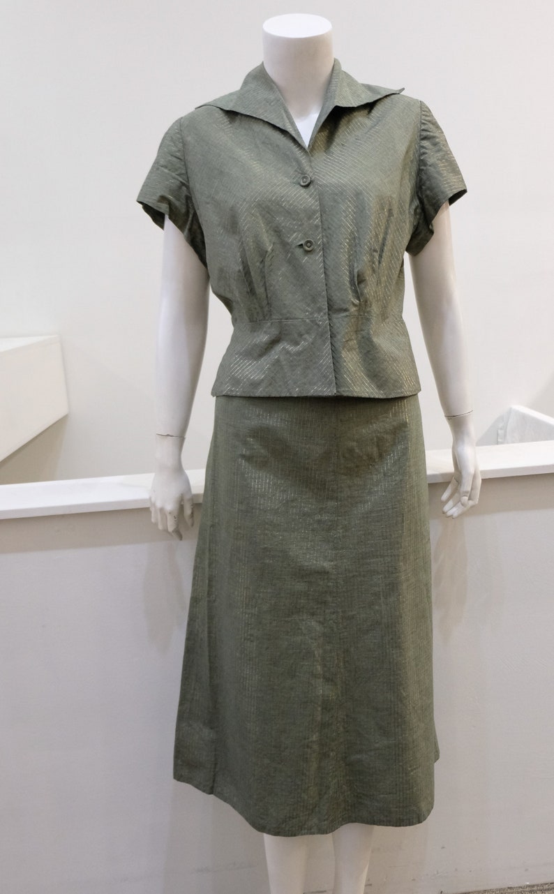 May include: A green, short-sleeved blouse with a collar and a matching skirt. The fabric has a subtle shimmer.