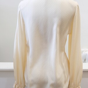 May include: A white long-sleeved blouse with a small white polka dot pattern. The blouse has a ruffled collar and cuffs.