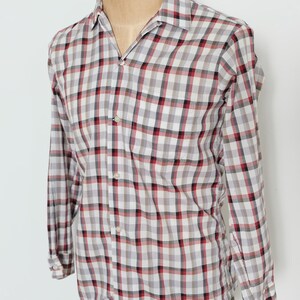 May include: A long-sleeved, button-down shirt in a classic plaid pattern. The shirt features a white base with a grid of red, black, and gray squares. The shirt is displayed on a mannequin.