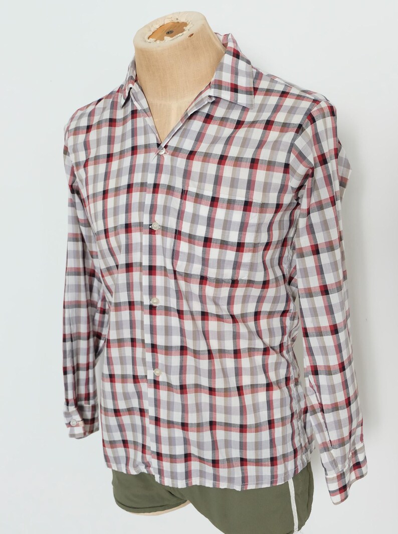 May include: A long-sleeved, button-down shirt in a classic plaid pattern. The shirt features a white base with a grid of red, black, and gray squares. The shirt is displayed on a mannequin.