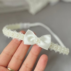 May include: A white headband with a satin bow and pearl embellishments.