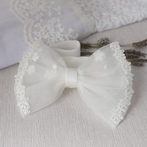 May include: White tulle bow with a delicate lace trim. The bow is tied with a white satin ribbon.