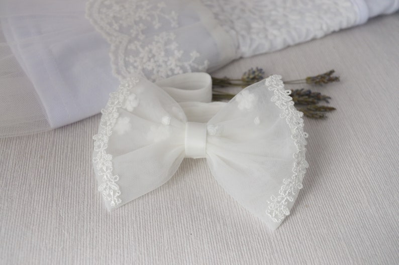 May include: White tulle bow with a delicate lace trim. The bow is tied with a white satin ribbon.