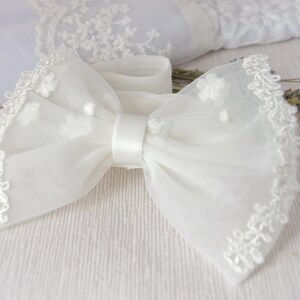 May include: A white tulle bow with a satin center and lace trim. The bow is tied with a white ribbon.