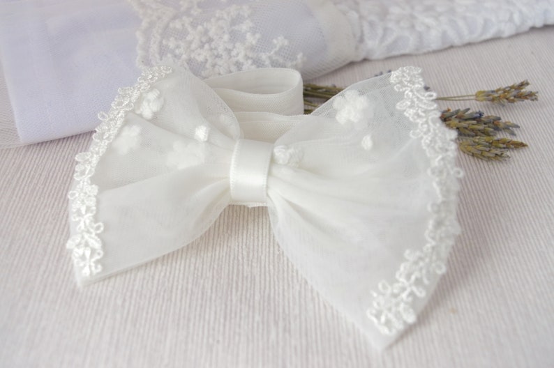 May include: A white tulle bow with a satin center and lace trim. The bow is tied with a white ribbon.