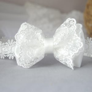May include: White lace headband with a large white bow. The headband is made of delicate lace and the bow is made of satin.