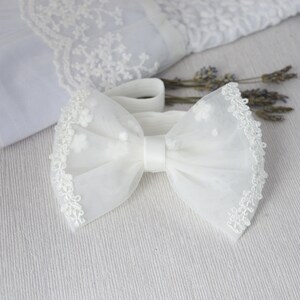 May include: White tulle bow with a delicate lace trim. The bow is tied with a white satin ribbon.
