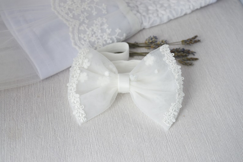 May include: White tulle bow with a delicate lace trim. The bow is tied with a white satin ribbon.