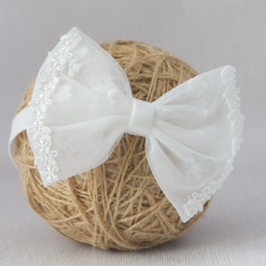May include: White lace bow headband with a delicate floral pattern. The headband is made of soft, sheer fabric and is perfect for adding a touch of elegance to any outfit.