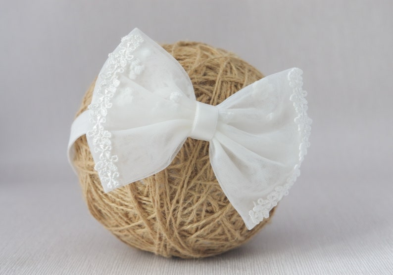 May include: White lace bow headband with a delicate floral pattern. The headband is made of soft, sheer fabric and is perfect for adding a touch of elegance to any outfit.