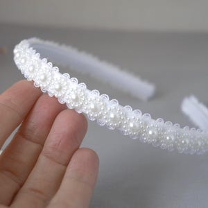 May include: A white headband with a row of faux pearls and a delicate floral design.