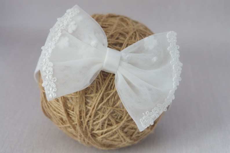 May include: A white tulle bow with a white lace trim. The bow is tied with a white satin ribbon and is sitting on a ball of twine.