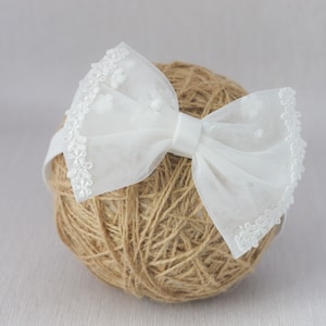 May include: White tulle bow headband with a delicate lace trim. The bow is tied in a simple knot and the headband is made of a soft elastic material.