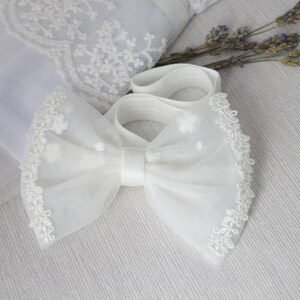 May include: White tulle bow with a lace trim and a satin center. The bow is tied with a white elastic band.