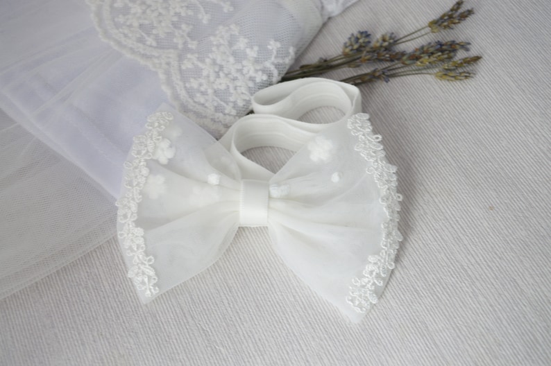 May include: White tulle bow with a lace trim and a satin center. The bow is tied with a white elastic band.