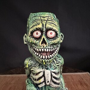 May include: Green zombie tiki mug with red eyes and a dripping green slime effect. The mug has a detailed skeletal ribcage and a grinning mouth.